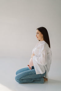 Cute young pregnant girl sitting on the white studio in warm light