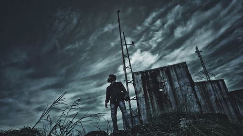 Low angle view of man standing against cloudy sky