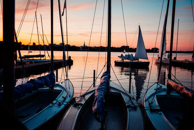 Sailboats moored at harbor against sky during sunset