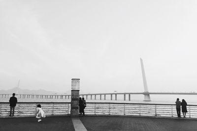 People on bridge over sea against sky