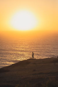Silhouette woman standing at beach against sky during sunset