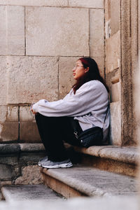 Portrait of young woman sitting against wall