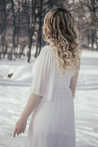 Rear view of young woman while standing on snow covered field