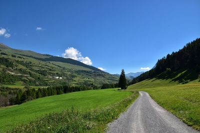 Road amidst green landscape against clear blue sky