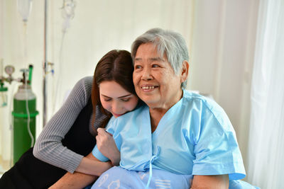 Granddaughter sitting by ill grandmother in hospital ward