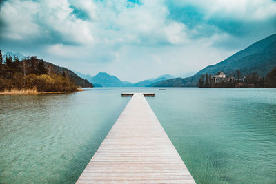 Boardwalk on sea against cloudy sky