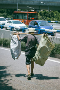 Rear view of man carrying metal in sacks on street