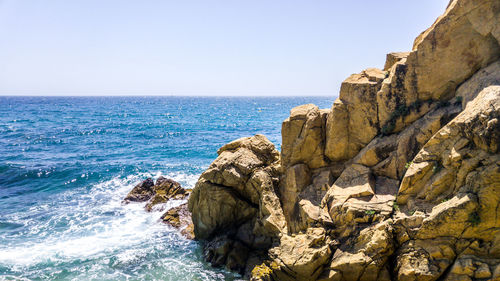 Scenic view of cliff by sea against clear sky