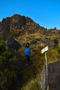 Rear view of man walking on mountain against clear blue sky
