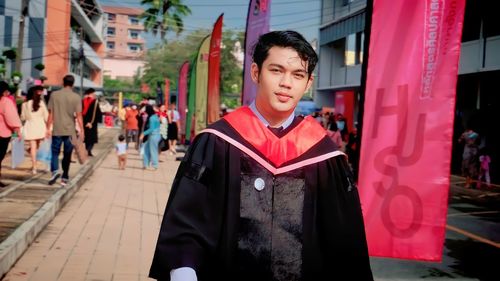 Portrait of young woman wearing graduation gown standing in city