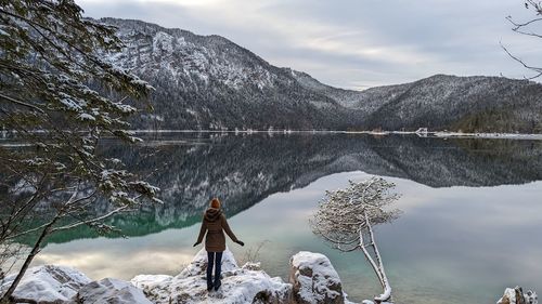 Rear view of woman standing on snow covered mountain against lake mountain and sky