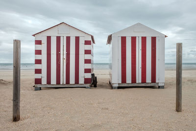 Two colourful beach huts on a deserted beach against cloudy sky