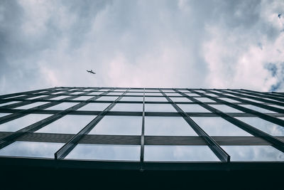 Low angle view of bird flying over building against cloudy sky