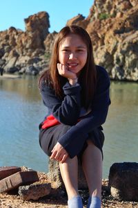 Portrait of a smiling young woman sitting on rock