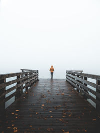 Rear view of man standing on pier during foggy weather