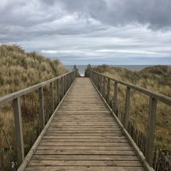 Wooden footbridge over sea against sky
