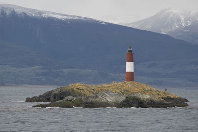 Lighthouse on sea by mountain against sky