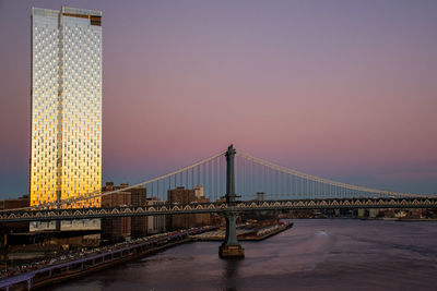Suspension bridge and building over river during sunset