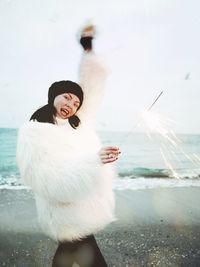 Portrait of cheerful woman holding burning sparkler at beach