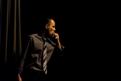 Young man looking away while standing against black background