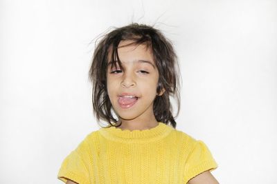 Portrait of girl sticking out tongue while standing against white background
