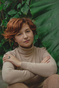 A beautiful plus size girl with red hair among the lush green branches of tropical plants. 