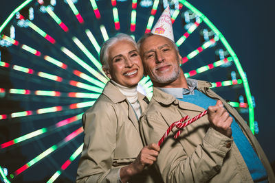 Portrait of happy couple standing against illuminated ferris wheel at night