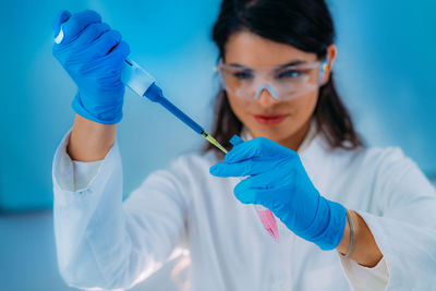 Student in white coat, working in research laboratory using micro pipette and test tube