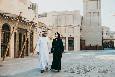 Full length of smiling couple talking while walking on street in town