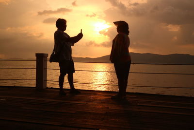 Silhouette friends standing against orange sky