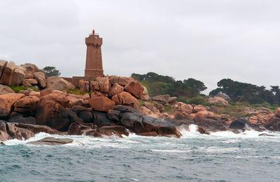 Lighthouse on rocks by sea against sky