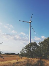 Low angle view of wind turbines on field against sky