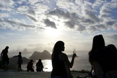 Silhouette people enjoying by sea against cloudy sky on sunny day