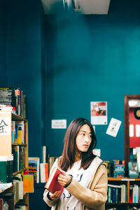 Portrait of young woman standing against book