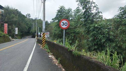 Road sign by trees against sky