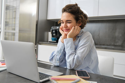 Young woman using phone while sitting on table