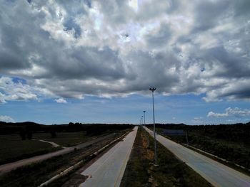 Road passing through field against sky
