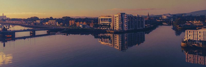 Bridge over river by buildings in city against sky during sunset