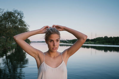 Young woman standing by lake against clear sky