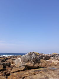 Rock formations on shore against clear blue sky