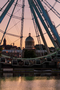 Bridge over river by buildings in city against sky at sunset