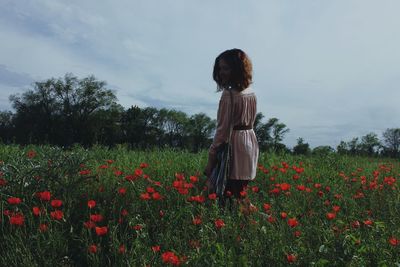 Woman standing amidst poppies on field