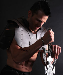 Close-up of warrior holding sword against black background