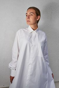 Young woman looking away while standing against white wall