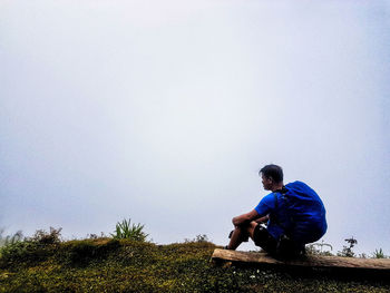 Young man sitting on plants against clear sky