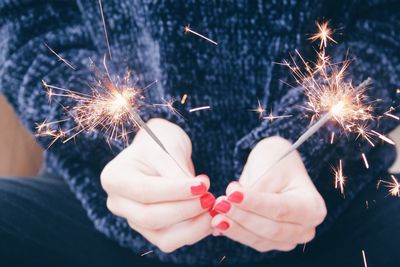 Midsection of woman holding sparkler at night