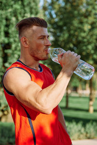 Side view of man drinking water while standing outdoors
