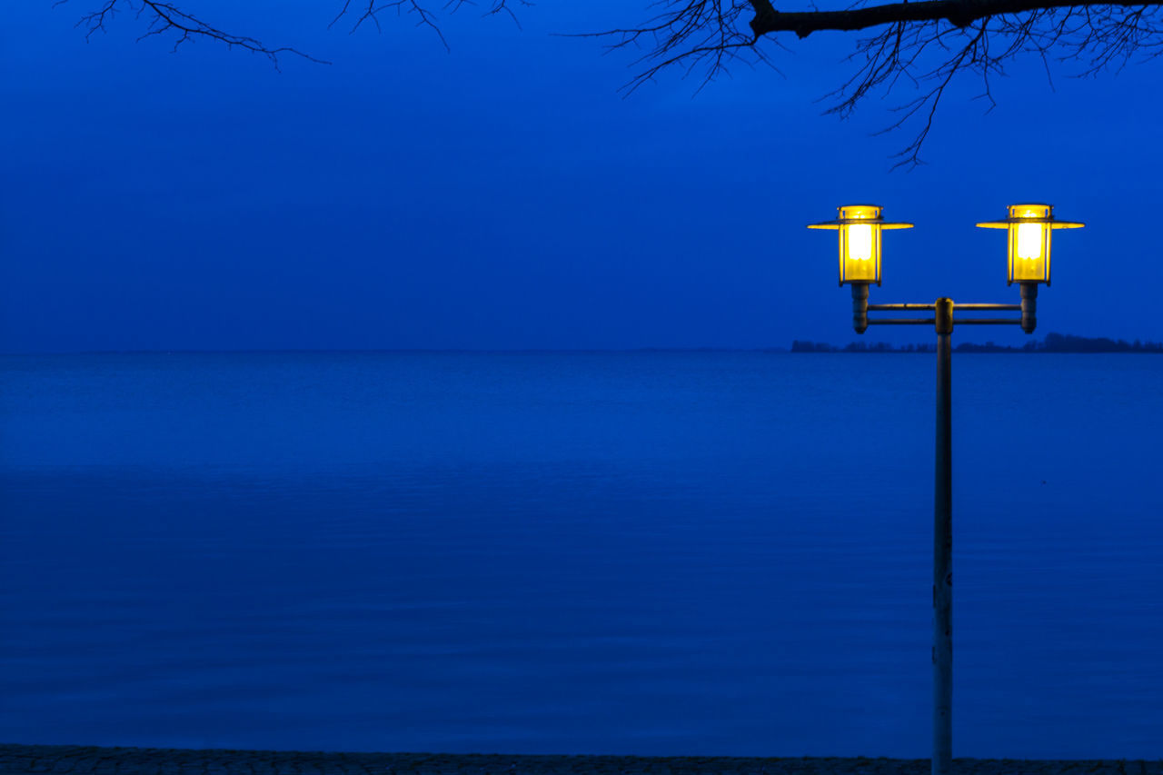 ILLUMINATED LAMP BY SEA AGAINST CLEAR BLUE SKY