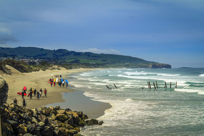 Surfers carrying surfboard at beach against blue sky