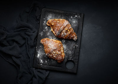 Baked croissants on a black wooden board sprinkled with powdered sugar, top view